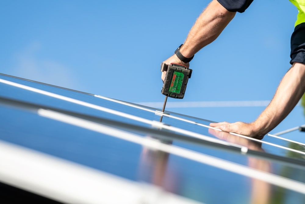 Unidentified electrician installing solar panels on the house roof using cordless screwdriver
