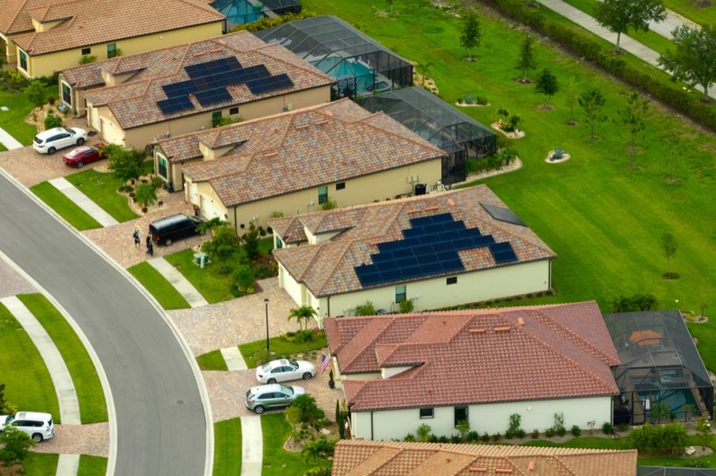 Aerial view of tightly located family houses with solar panels on roofs in Florida closed suburban area. 