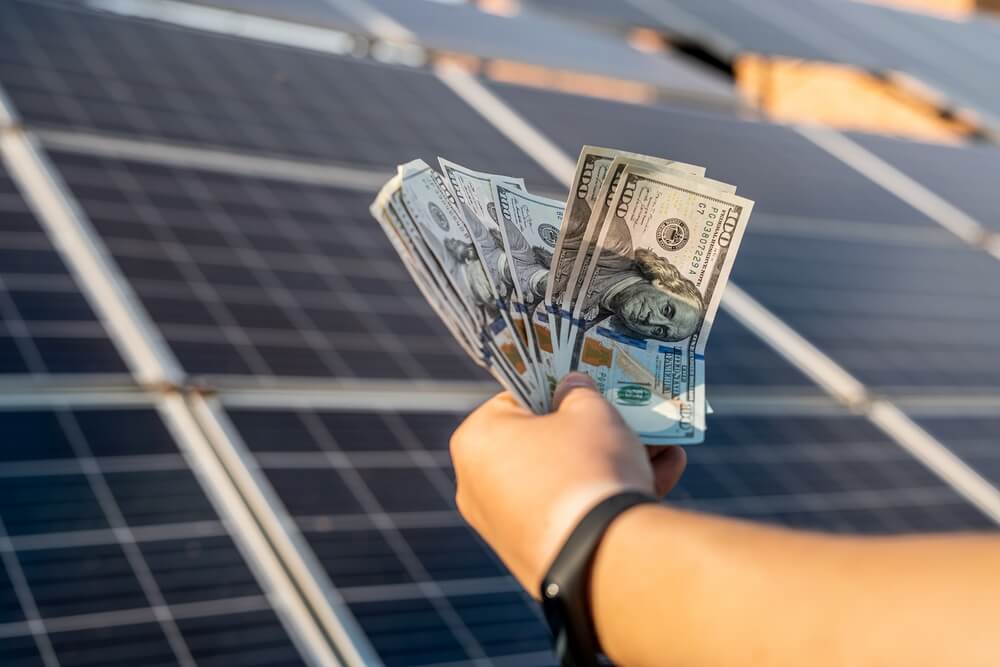 Saving money with sun energy and solar panels. Hand with dollars

