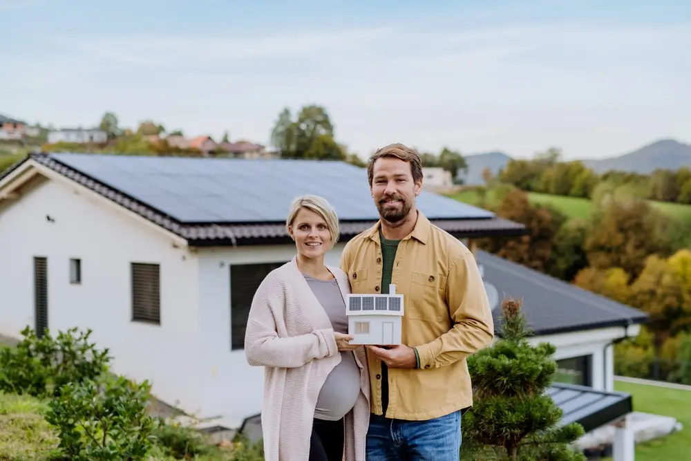 Close up of happy couple holding paper model of house with solar panels.